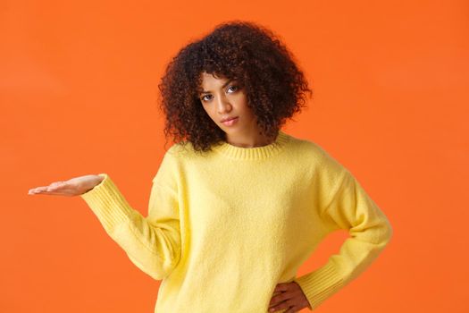 So what, I dont care. Unbothered and careless unimpressed sulking african-american woman with curly hair, raise hand in dismay displeased with bad result, dont give a damn, orange background.