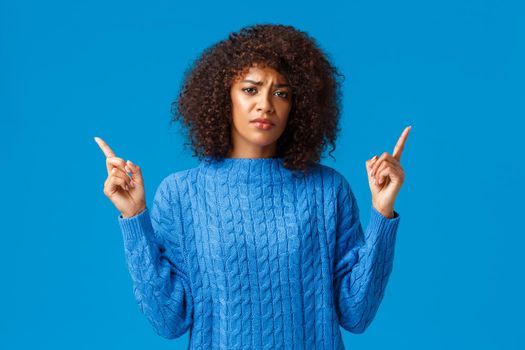 Girl talking about bad experience feeling uneasy and upset. Grimacing cute gloomy african-american woman with afro haircut, frowning indecisive and displeased, pointing fingers up.