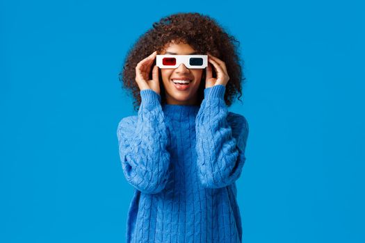 Lets watch and chill. Happy charismatic african-american female enjoying premiere new awesome movie, put on 3d glasses go cinema and smiling as looking screen fascinated, standing blue background.