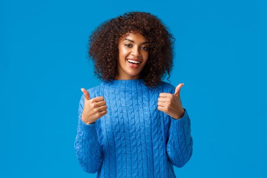 Everything super cool. Cheerful and satisfied african american woman with afro haircut, smiling and showing thumbs-up in approval, like product, recommend software or app, standing blue background.