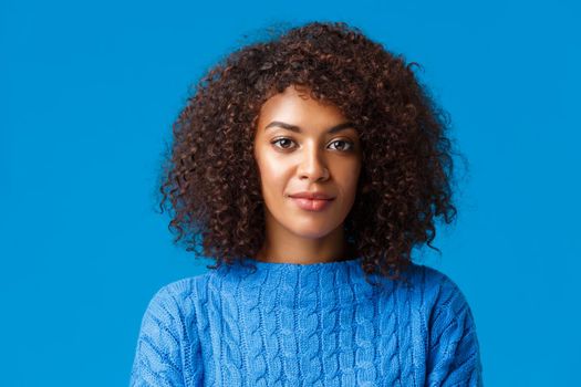 Close-up portrait calm and carefree good-looking african american female in sweater, with afro curly hairstyle, smiling cute and looking camera with friendly pleasant expression, blue background.