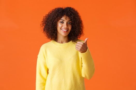 You should come and see it. Carefree good-looking hipster girl yellow sweater, inviting come inside pointing thumb behind herself and smiling, recommend product or company service, orange background.