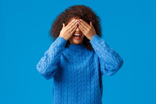 Girl playing with siblings in hide-n-seek, counting ten start seeking. Charismatic lovely african american woman close eyes as waiting surprise or make peekaboo gesture, blue background.