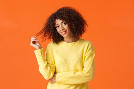Waist-up portrait sassy and coquettish good-looking african american woman rolling curl in fingers tilt head and checking-out someone with cheeky flirty smile, standing orange background.