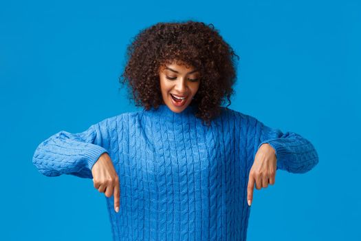 Time for shopping, lets get it. Excited and happy, lovely african-american woman with afro haircut, looking and pointing down amused, with cheerful carefree smile, standing blue background.