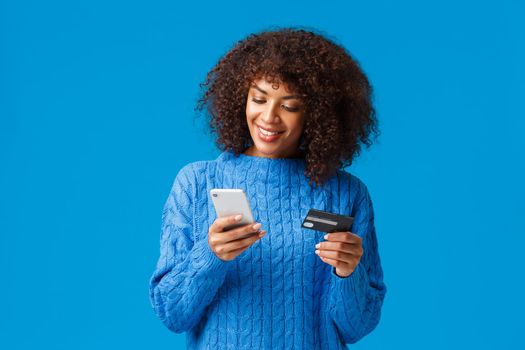 Shopping, holidays and presents concept. Attractive smiling african-american woman paying for online purchase, buying gifts in internet, holding credit card and smartphone, submit payment.