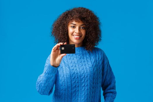 Banking, shopping and finance concept. Attractive pleasant african-american woman with afro hair, winter sweater, showing credit card, paying online purchase, prepare for holidays.