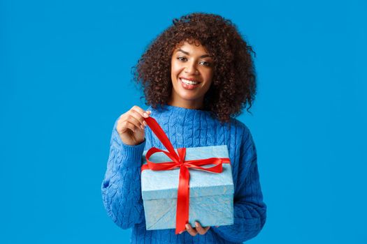 Happiness, holidays and family concept. Happy smiling charming african-american woman with afro haircut, unwrapping gift, pulling knot and smiling cheerful receiving present on new year.