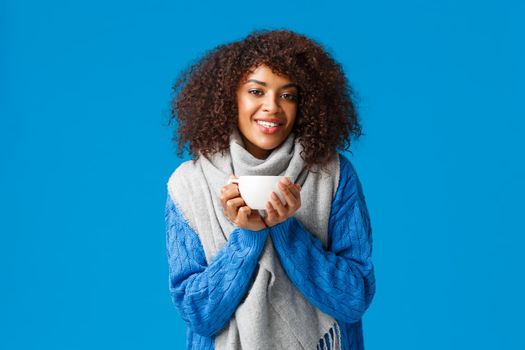 Comfort, tenderness and warmth concept. Charming lovely african american woman with afro haircut, in sweater and scarf, warming up with nice cup tea, enjoying hot coffee, smiling camera.