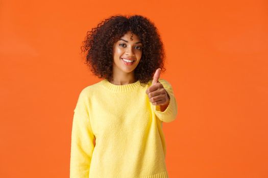 Waist-up portrait cheerful satisfied girl made her final choice, showing thumb-up in approval or like, recommend product, nod agreement, smiling delighted, standing orange background.