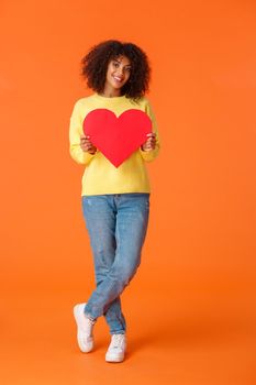 Full-length vertical shot lovely, romantic and cute stylish young african-american woman looking camera and holding big red heart card to express love, happy valentines day, confess sympathy.