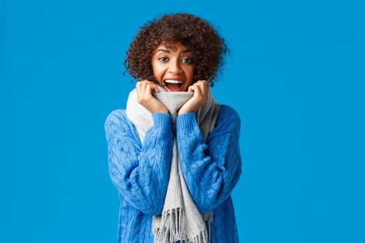 Happy holidays, finally snow and beautiful winter season came. Cheerful upbeat charismatic african-american female in sweater and warm scarf, laughing and smiling joyfully, blue background.