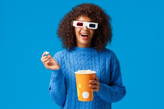 Leisure, lifestyle and modern people concept. Carefree relaxed and joyful, smiling african american woman with afro hairstyle, eating popcorn in cinema, wear 3d glasses and smiling watching movie.