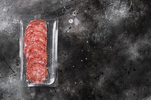 Smoked salami sausages slices in vacuum pack set, on black dark stone table background, top view flat lay, with copy space for text