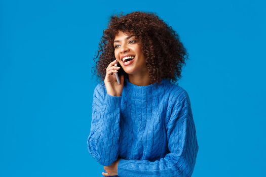 Charismatic attractive happy african-american woman answering phone, laughing happily and smiling, holding smartphone near ear, standing blue background joyful, wishing happy holidays.