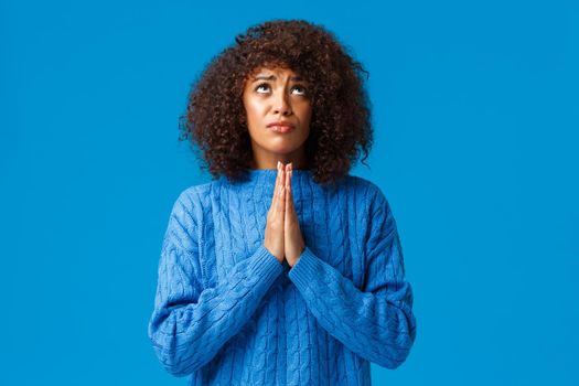 God please help find way. Supplicating faithful and hopeful young african-american woman in need, press hands together and pray looking up sky searching mercy or wayout, standing blue background.