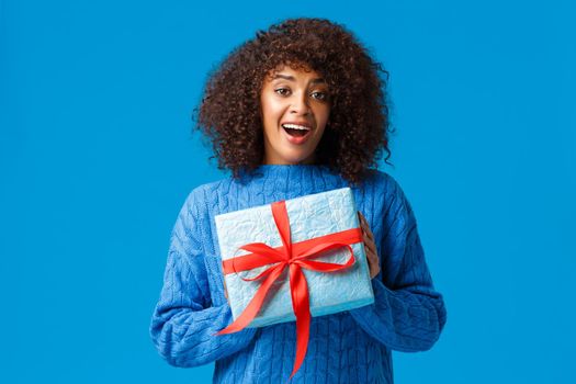 Girl cant wait unwrap gifts on winter holiday season. Cute and lovely girlfriend african american female holding wrapped present and smiling, thanking standing blue background.