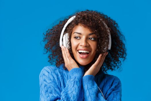 Close-up portrait cheeky and carefree happy smiling african-american modern gen-z girl with afro haircut, curly hair, listen music in headphones smiling delighted, enjoy new earphones.