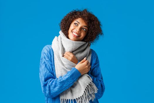 Dreamy romantic and carefree african american woman in winter sweater, scarf, looking up thoughtful, imaging what present boyfriend buy for valentines day, holiday celebration, blue background.