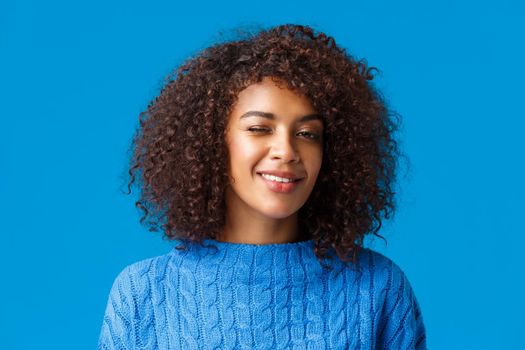 Everything be alright, relax and enjoy holidays. Cheerful cute and coquettish african american hipster girl with afro haircut, winking encourage all good, smiling, blue background.