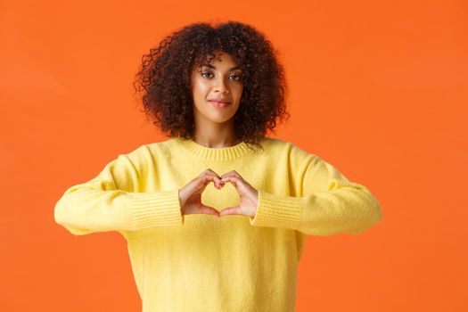 Love me for who I am. Caring and tender, lovely romantic african-american female express her feelings, showing heart gesture, confess love on valentines day, standing orange background happy.