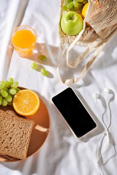 Summer picnic concept. Bread with fruit, bag, phone and ear[hone on white background