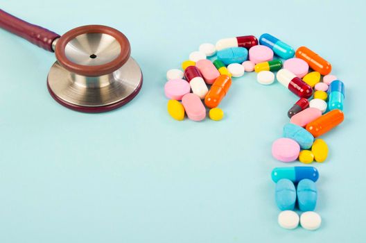 A question mark from laid out of medicine pills with stethoscope on blue background.