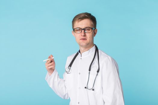 Stressed doctor smoking cigarettes on blue background.