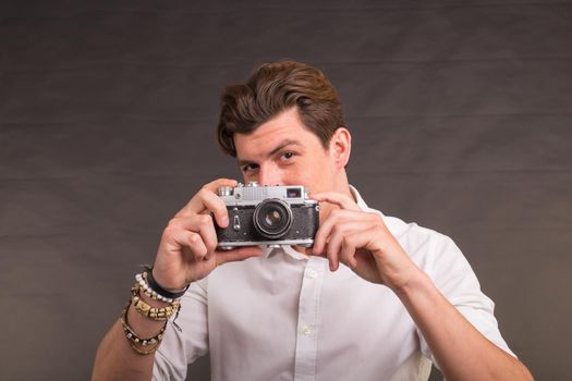 Technology, photography and hobby concept - man with retro camera, taking a photo of you over the grey background.