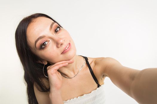 Close-up of young beautiful woman taking selfie on white background.