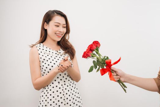 Cheerful charming young woman receiving bunch of flowers from her boyfriend over white background