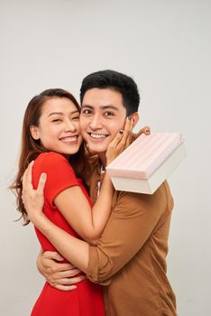 Happy young couple standing isolated over whitewbackground, celebrating, holding gift box, hugging