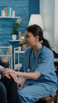 Nurse giving assistance to retired man with disability in nursing home. Invalid patient sitting in wheelchair, receiving support and help at healthcare checkup visit. Disabled person