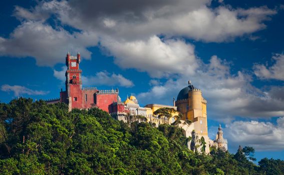 View of the Da Pena Palace in the Portuguese hilltop town of Sintra with blue sky and white clouds.