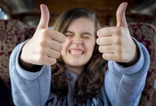 Long-haired teenage girl with her face out of focus in the background of the image and her hands with thumbs up in OK sign in the foreground.