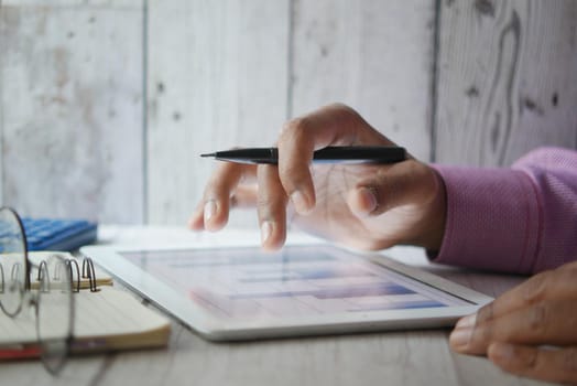 man's hand working on digital tablet at office desk, using self created chart.
