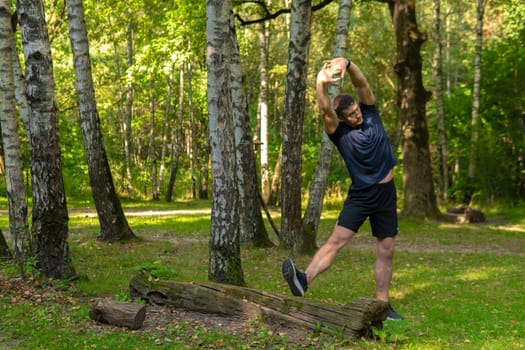 A young enduring athletic athlete is doing stretching in the forest outdoors, around the forest, oak trees.healthy athlete nature, lifestyle trail athletic wellness motion, wellbeing. Summer distance stretches