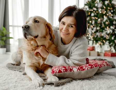 Girl with golden retriever dog lying on floor at home with Christmas tree. Young woman with pet doggy in festive time
