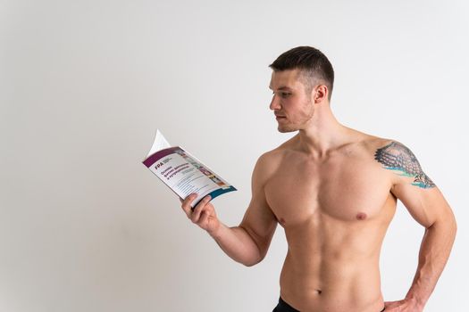 Bodybuilder reads the book on a white background isolated at the bottom of his head on his hands bodybuilder muscular, muscle fitness muscles, sexy sport. Health ABS holding, beach tan
