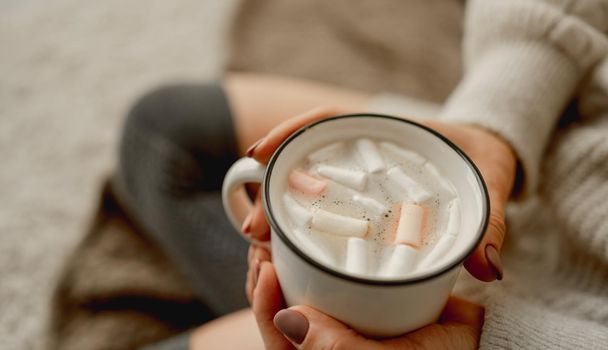 Girl hands holding mug filled with cocoa and marshmallow. Cozy closeup portrait of woman with warm beverage in cup in winter time