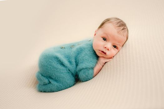 Newborn baby boy wearing knitted costume lying on his tummy and looking at camera. Cute infant child kid studio portrait