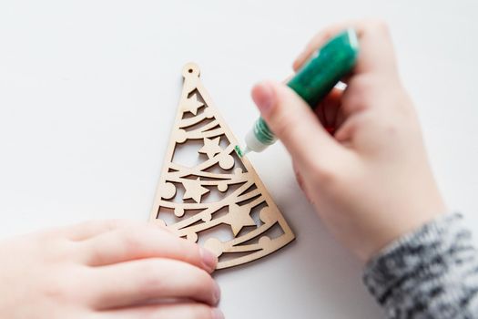 Little child painting wooden Christmas tree decorations sitting at table at home. Holiday DIY concept for children.