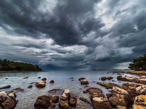 A big thunderstorm with dark black clouds breaks out at the rocky shore.