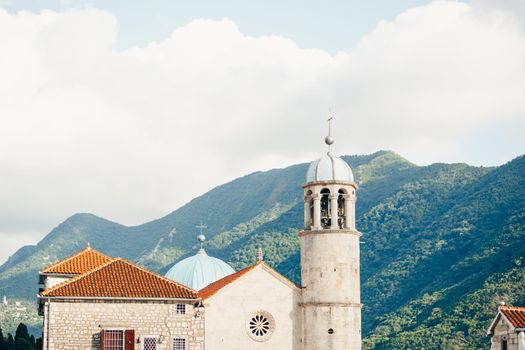 Church of Our Lady on the rocks on the island of Gospa od Skrpjela against the backdrop of mountains. High quality photo