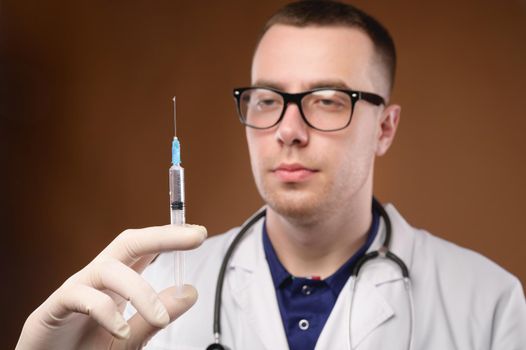 Young caucasian doctor man preparing to do a vaccination with a syringe. Studio shot on a brown background. Release air from the syringe before the injection.