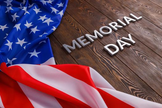the words memorial day laid with silver metal letters on wooden board surface with crumpled usa flag.