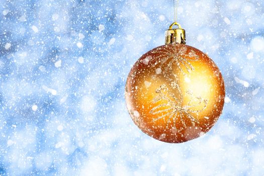 Golden Christmas ball in the snow on a blurred blue-gray background. Copy space. New year greeting card.