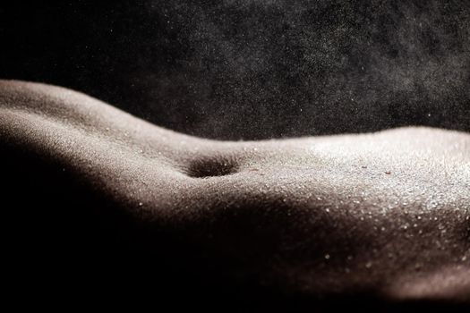 Close-up of drops of water falling on a woman's naked slender belly, black background. Soft focus. Non-Explicit Nudity.