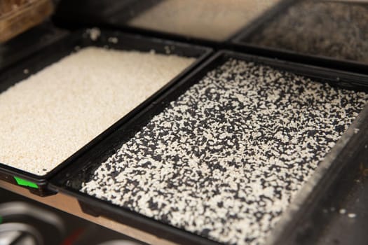 Plastic containers with white and black sesame seeds at the chef's workplace in a sushi restaurant