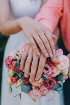 HONEYMOONS HANDS ON A WEDDING BOUQUET OF FLOWERS. Hands and rings on wedding bouquet. Bride and groom hold hands with gold wedding rings on a wedding bouquet of white and beige roses, close-up without faces. Hands of bride and groom with gold rings on a vintage wedding bouquet, close up. Concept of happy marriage day.